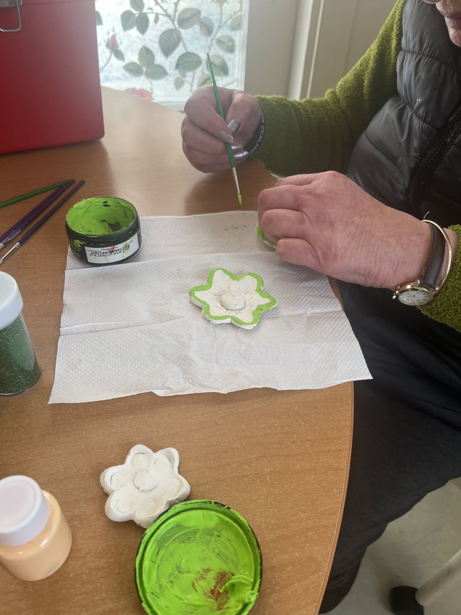 Close-up of a resident painting a small clay flower green.